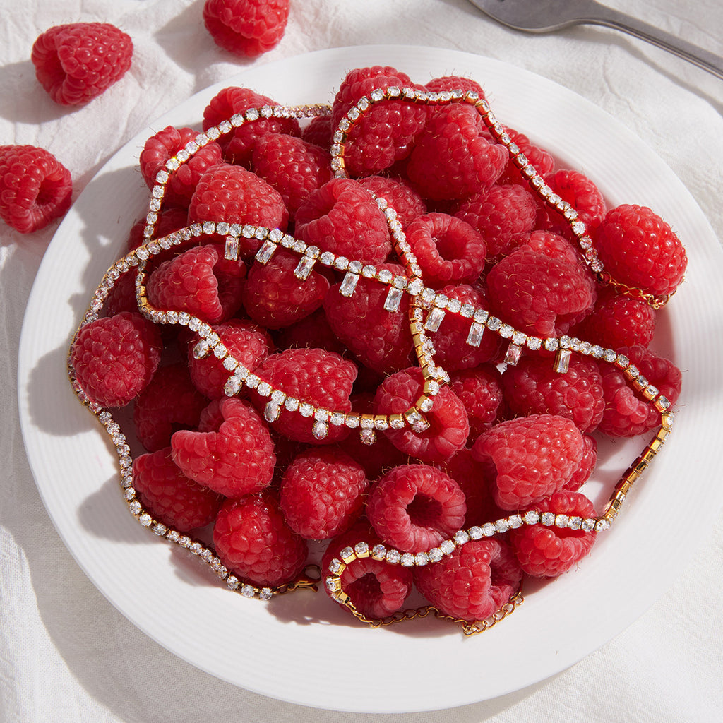 Two fringe necklace designs arranged on raspberries