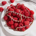 Two fringe necklace designs arranged on raspberries