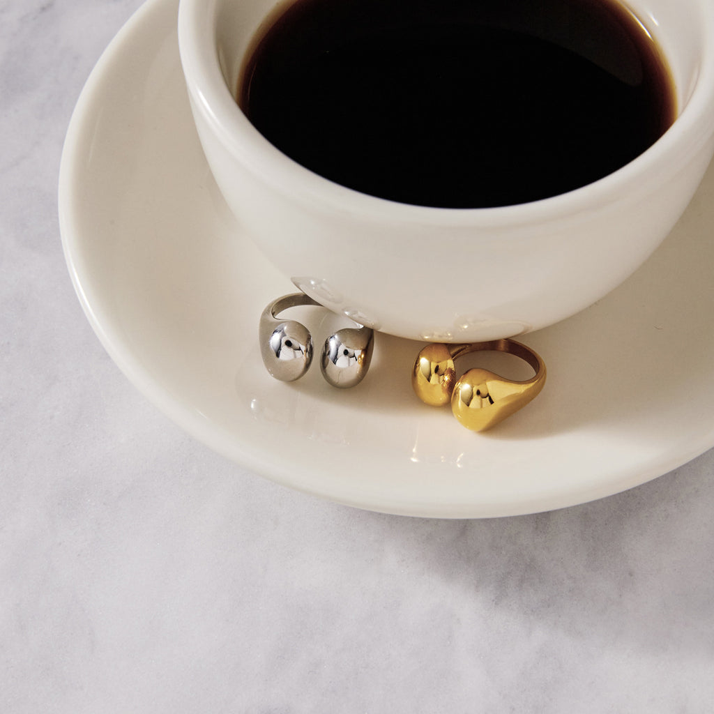 Two metal-color open rings displayed beside a cup