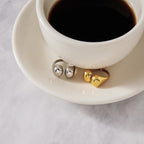 Two metal-color open rings displayed beside a cup