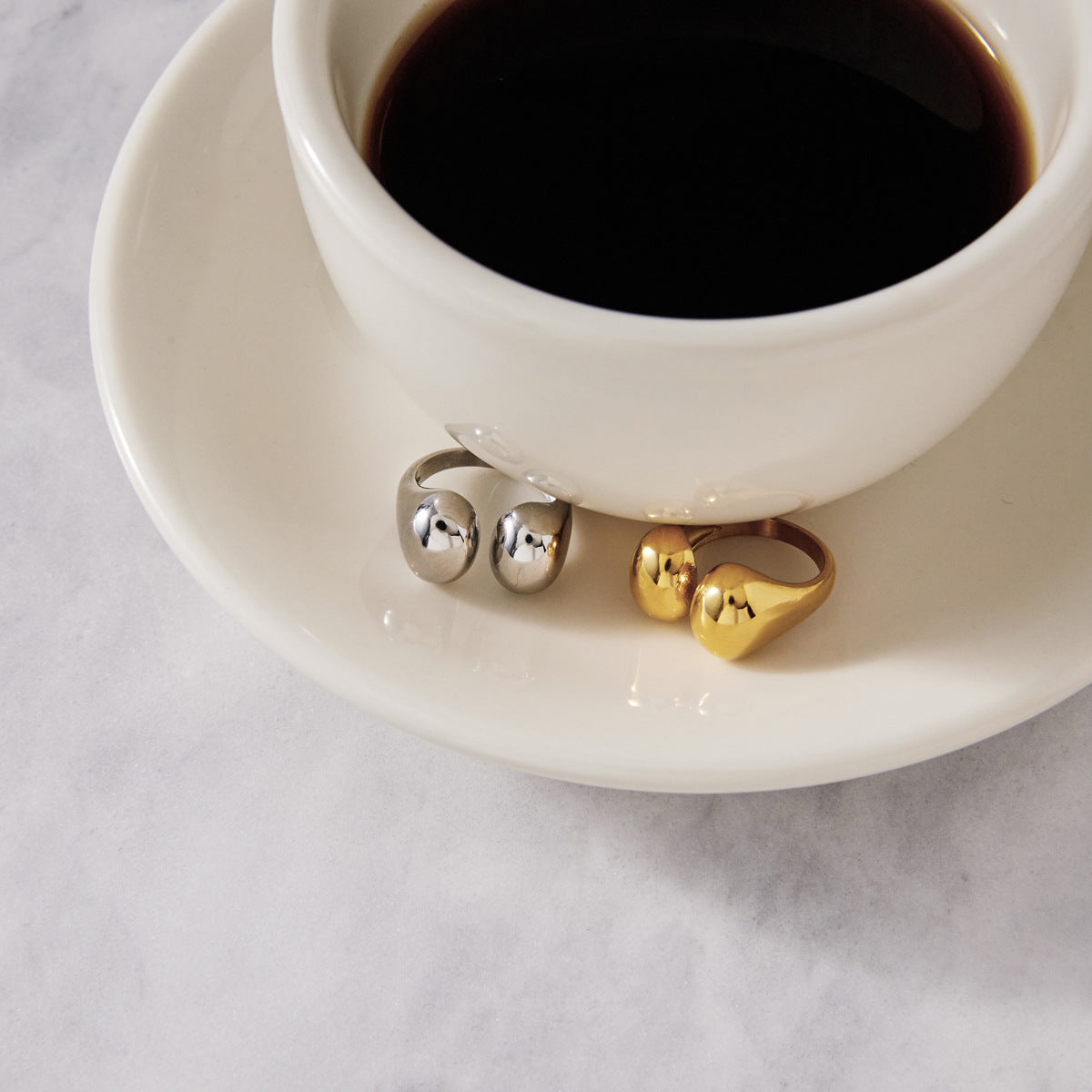 Two metal-color open rings displayed beside a cup