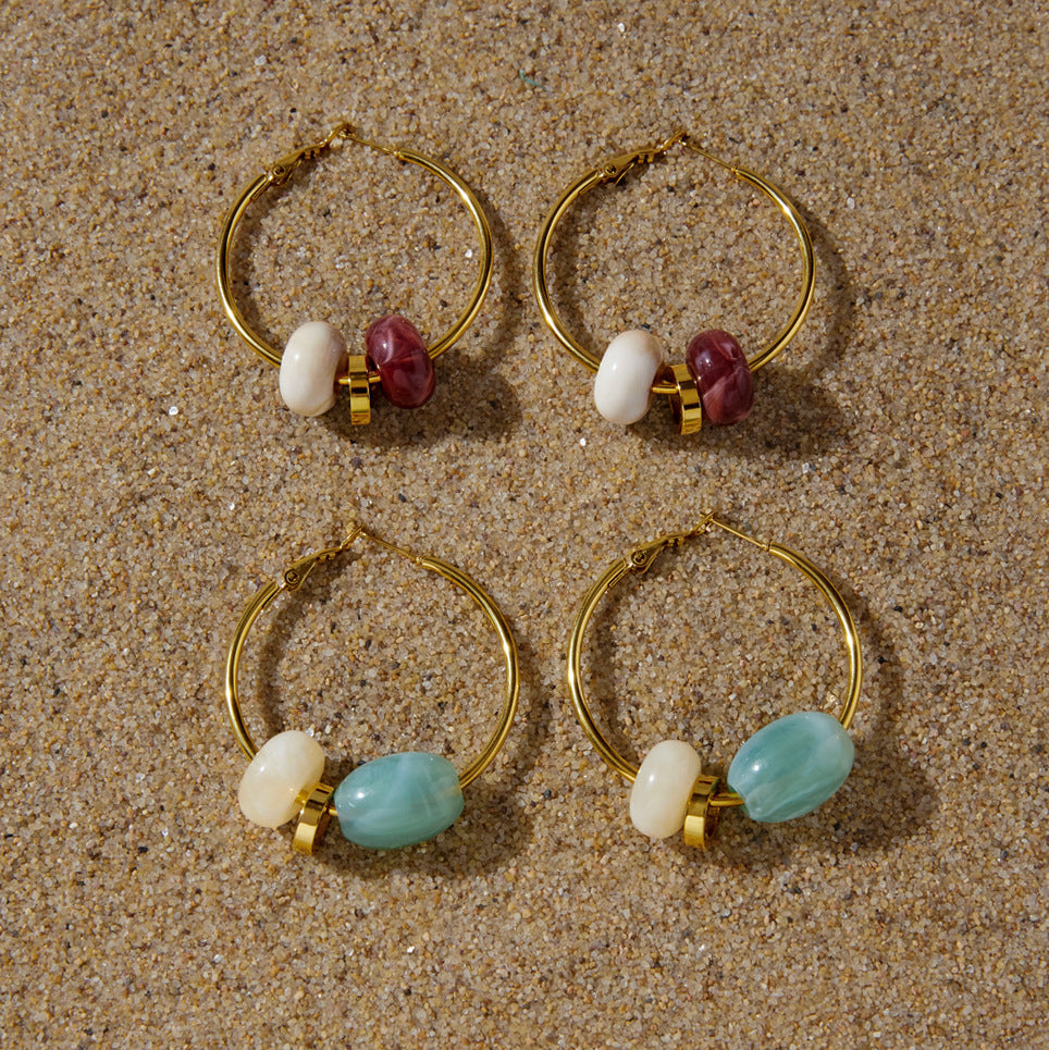 Burgundy and aqua resin bead hoops arranged on sand
