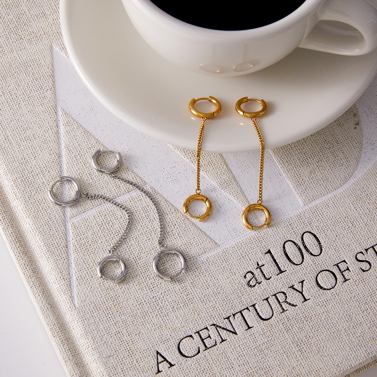double-huggie chain earrings in two finishes beside a coffee cup