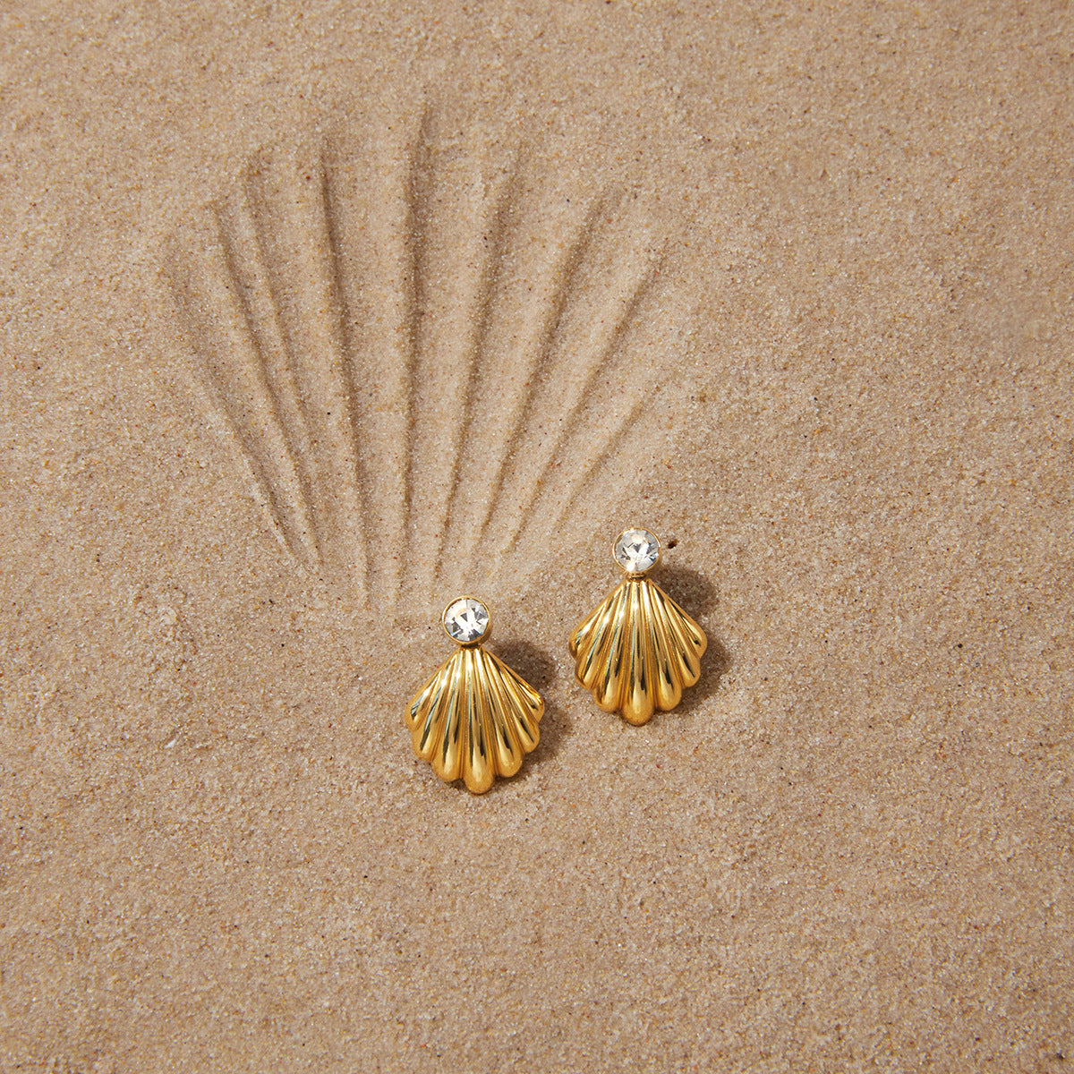 Fluted shell earrings arranged on sand