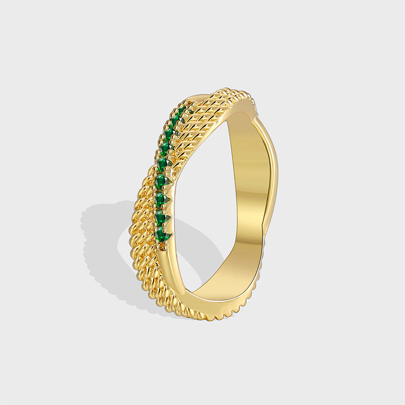 isolated gold plated brass crossover ring with small green stones