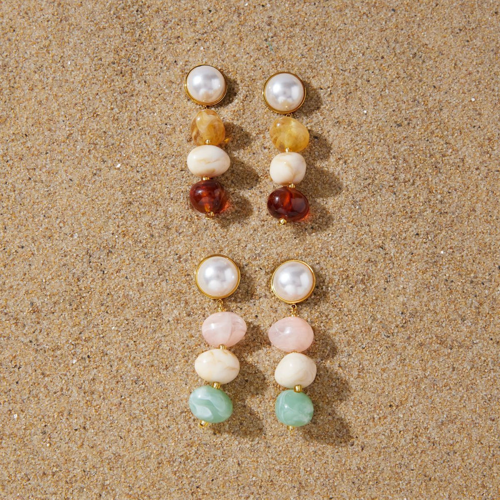 Warm and pastel three-bead earrings displayed on sand