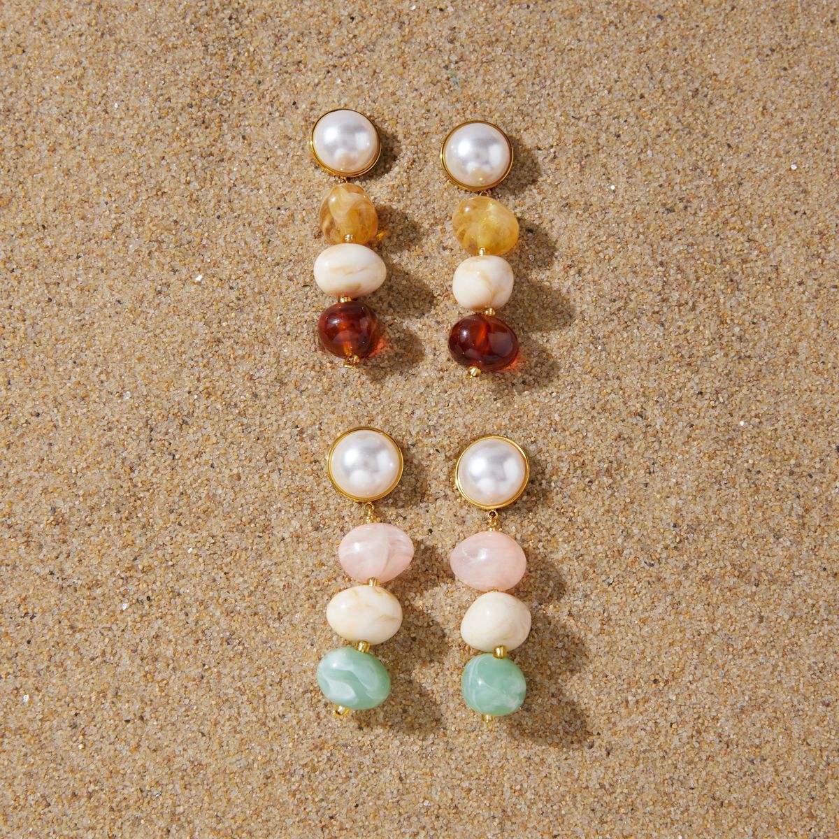 Warm and pastel three-bead earrings displayed on sand