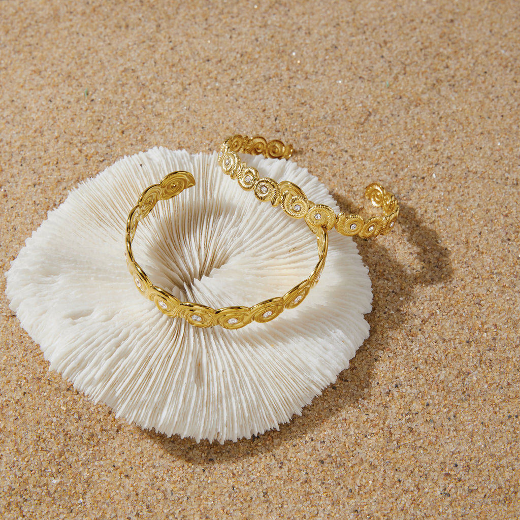 Gold-tone open cuffs resting on a pale shell