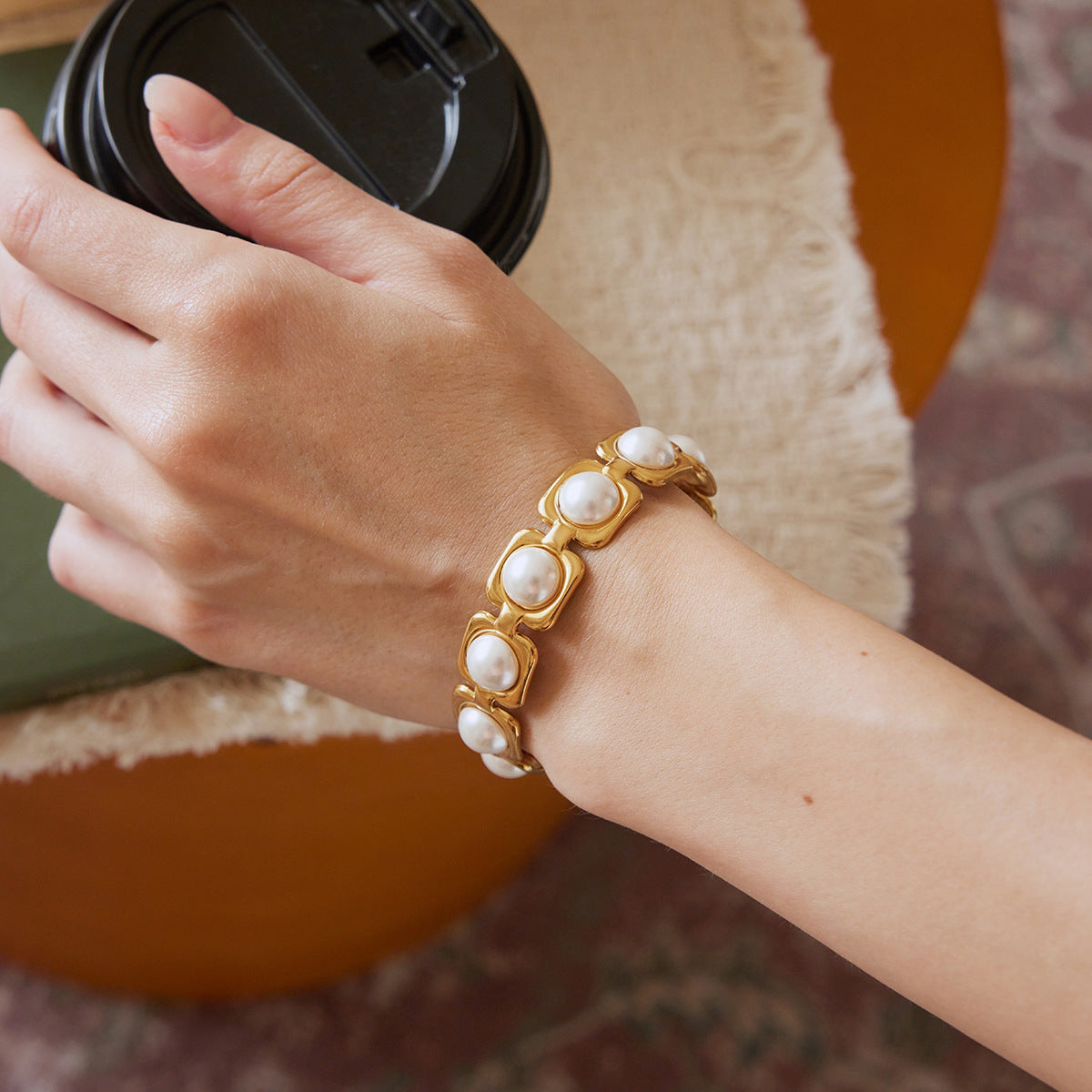 White bead open cuff bracelet worn while holding a cup
