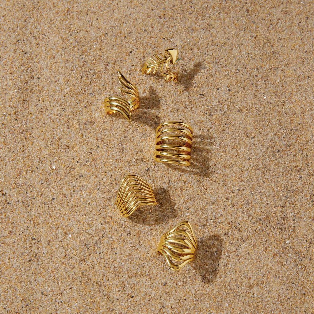 Gold-tone ring styling arrangement on sand