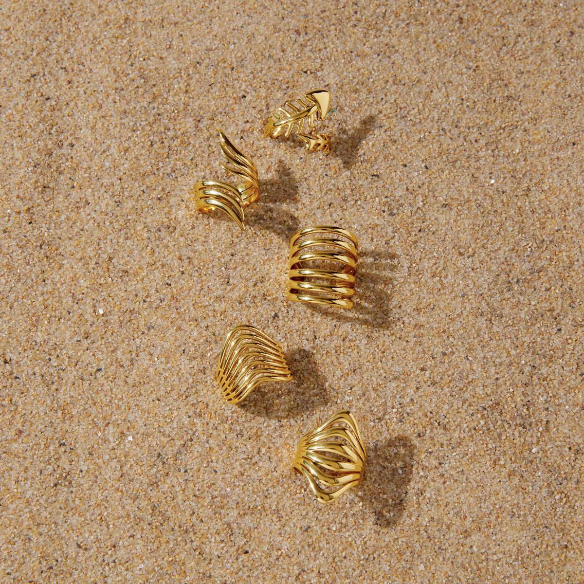 Gold-tone ring styling arrangement on sand