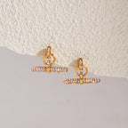Gold-tone rhinestone T-bar earrings on a ledge