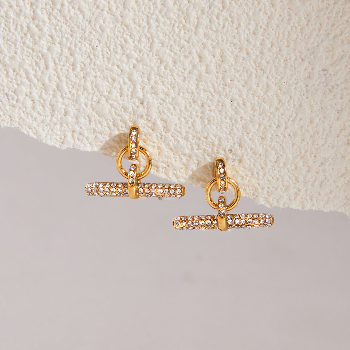 Gold-tone rhinestone T-bar earrings on a ledge