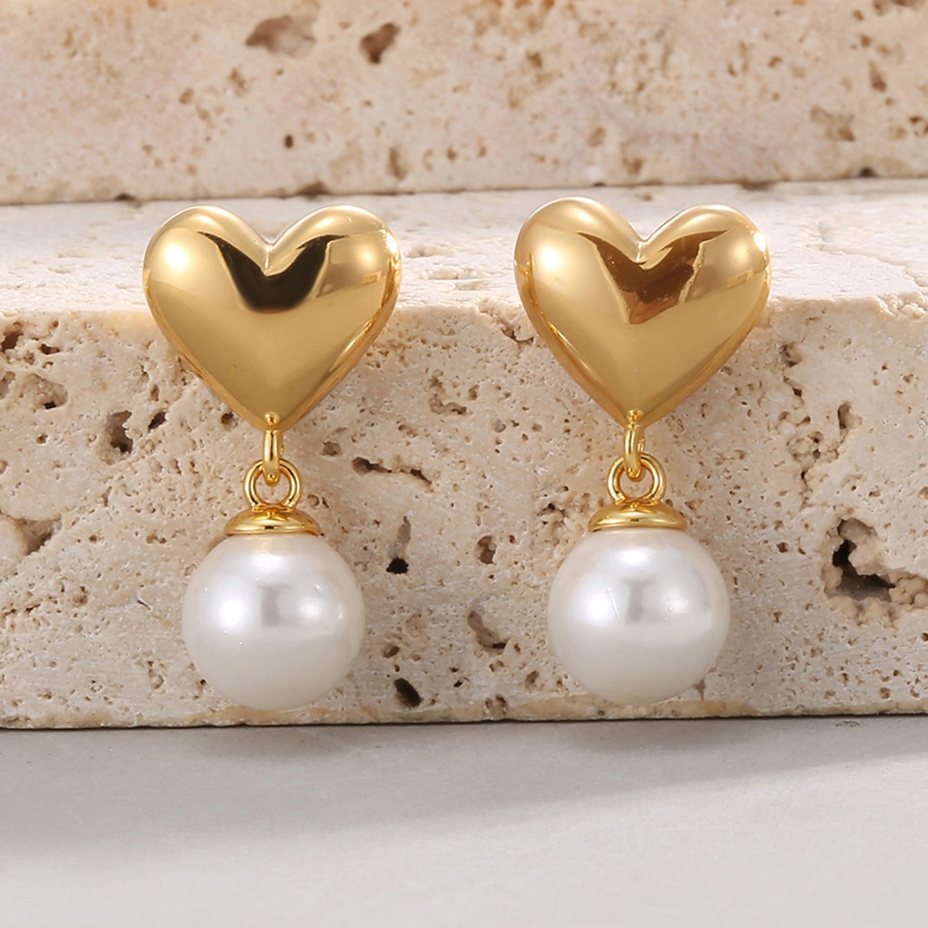 gold plated heart and white shell pearl drop earrings on stone