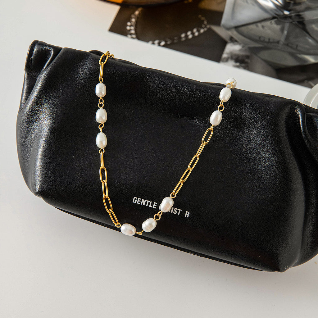 Gold plated pearl station chain displayed on a black bag