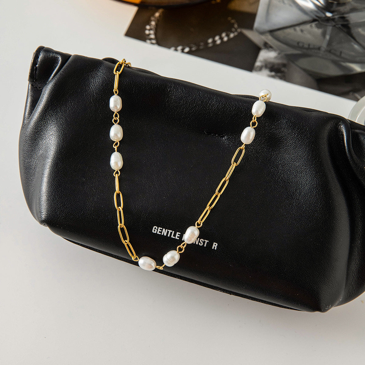 Gold plated pearl station chain displayed on a black bag