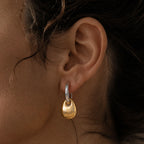 Silver tone hoop with gold tone pebble drop worn on an ear