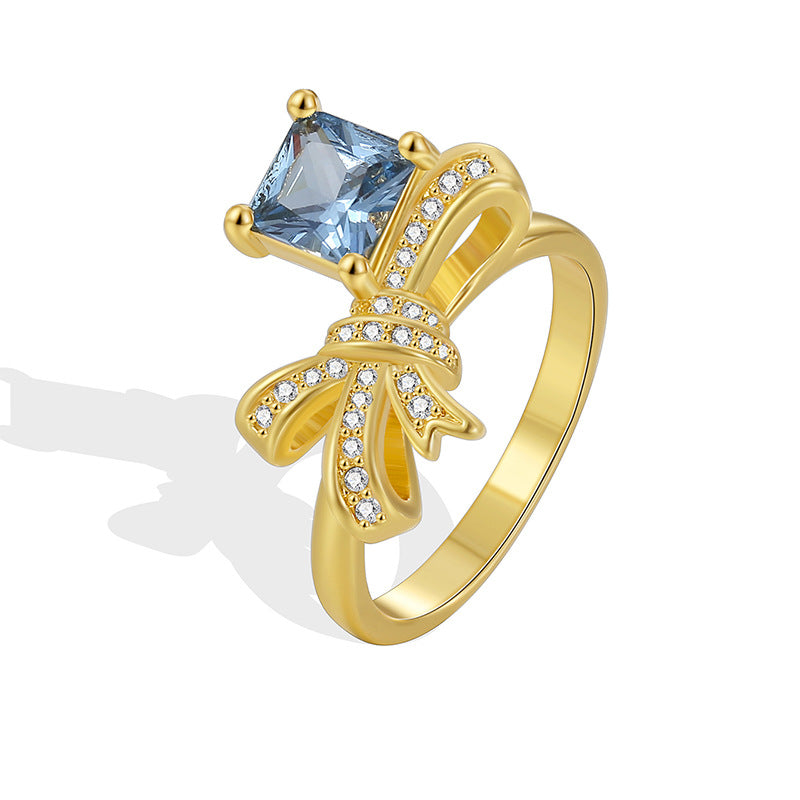 isolated gold plated bow ring with blue square center stone
