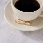 Gold-tone mixed-cut earrings beside a cup