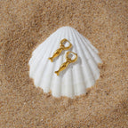 Gold tone fish earrings displayed on a scallop shell