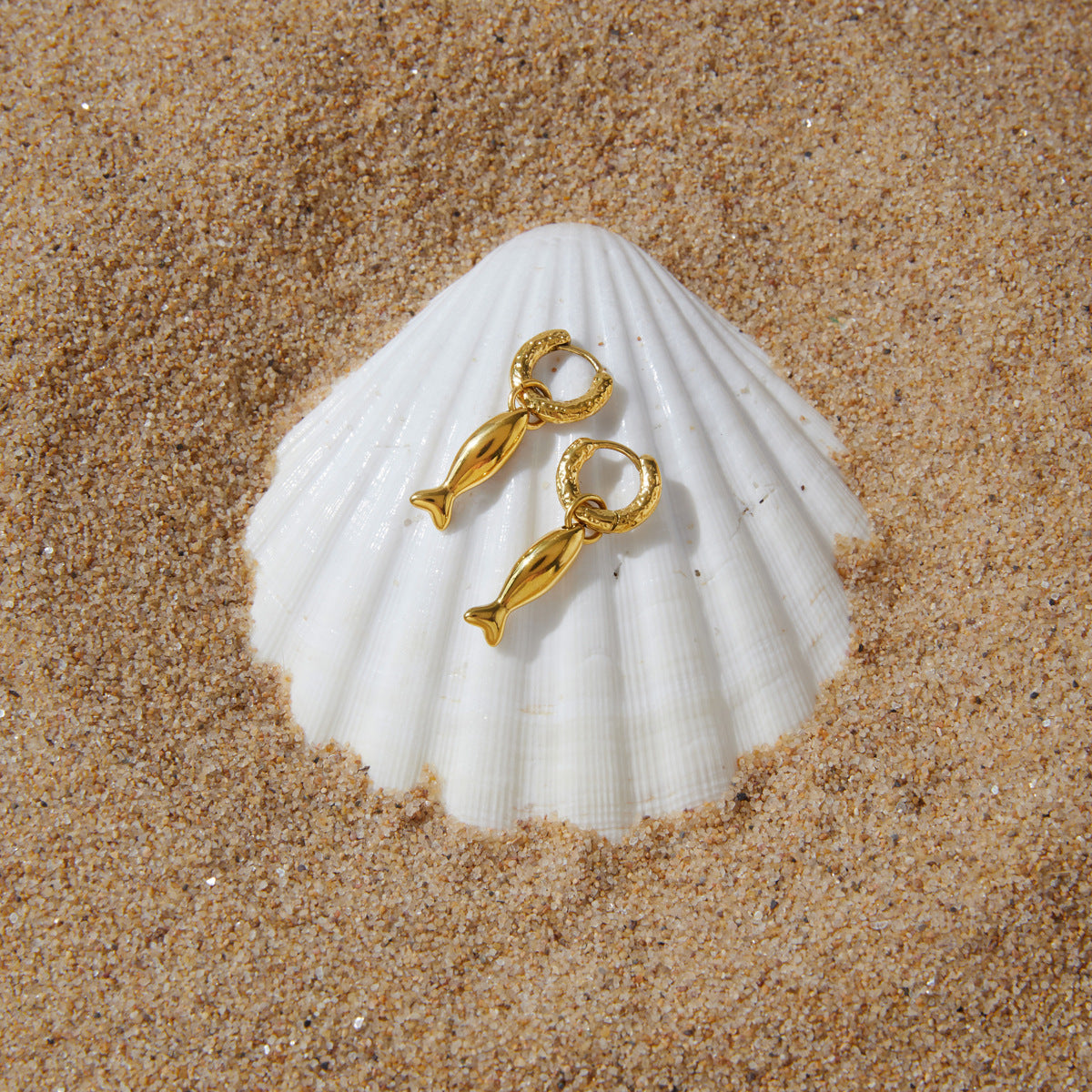 Gold tone fish earrings displayed on a scallop shell