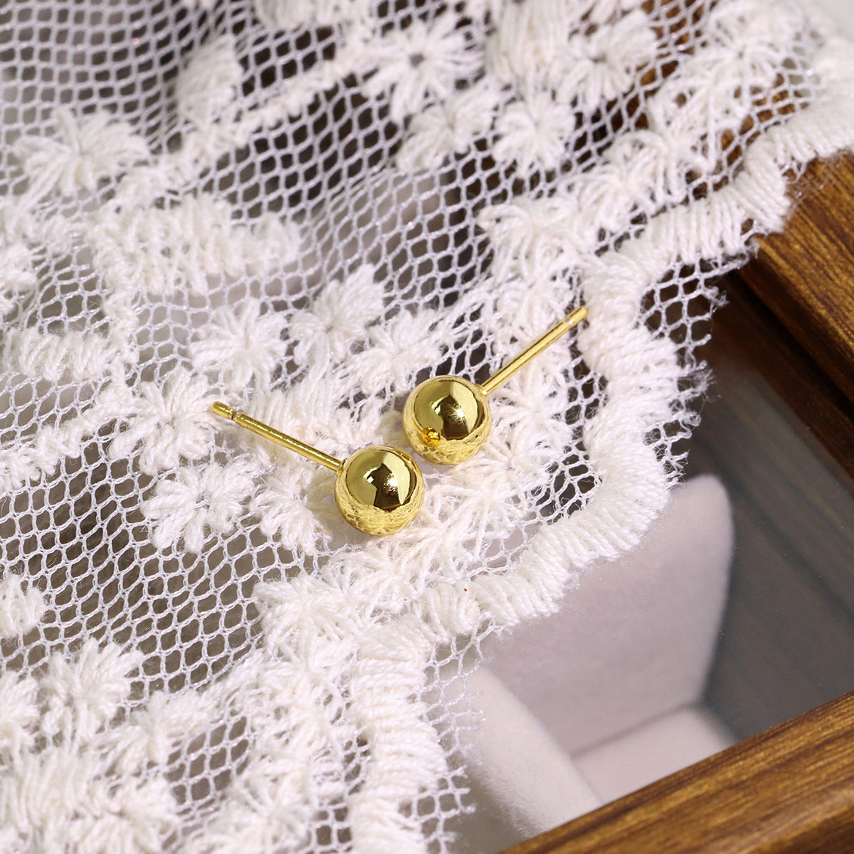gold plated spherical stud earrings on white lace