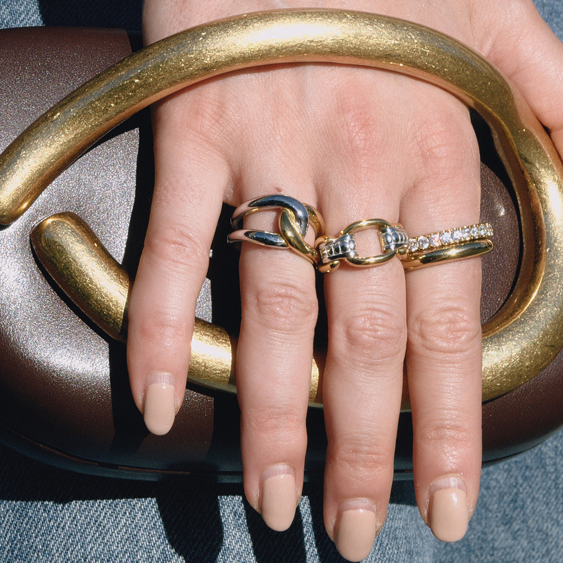 Two-tone link and crossover rings worn together on a hand
