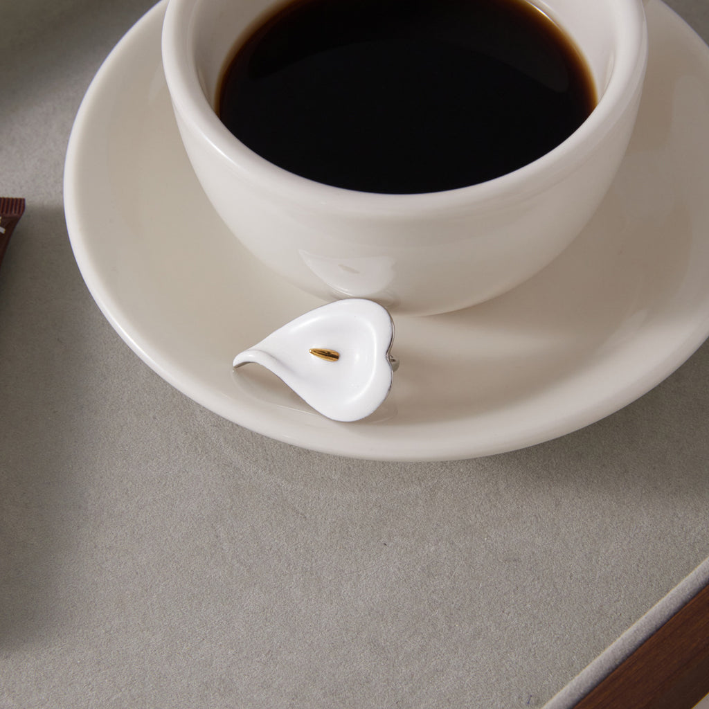 White flower ring displayed beside a coffee cup