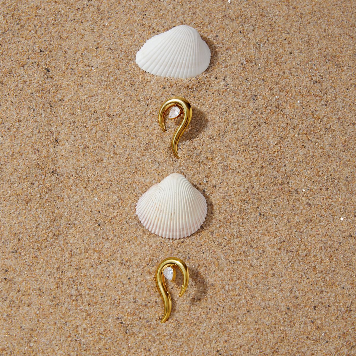 Gold-tone pointed earrings arranged on sand