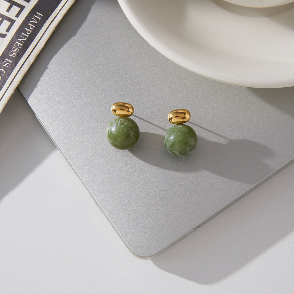 pair of marbled green resin sphere earrings on gray surface