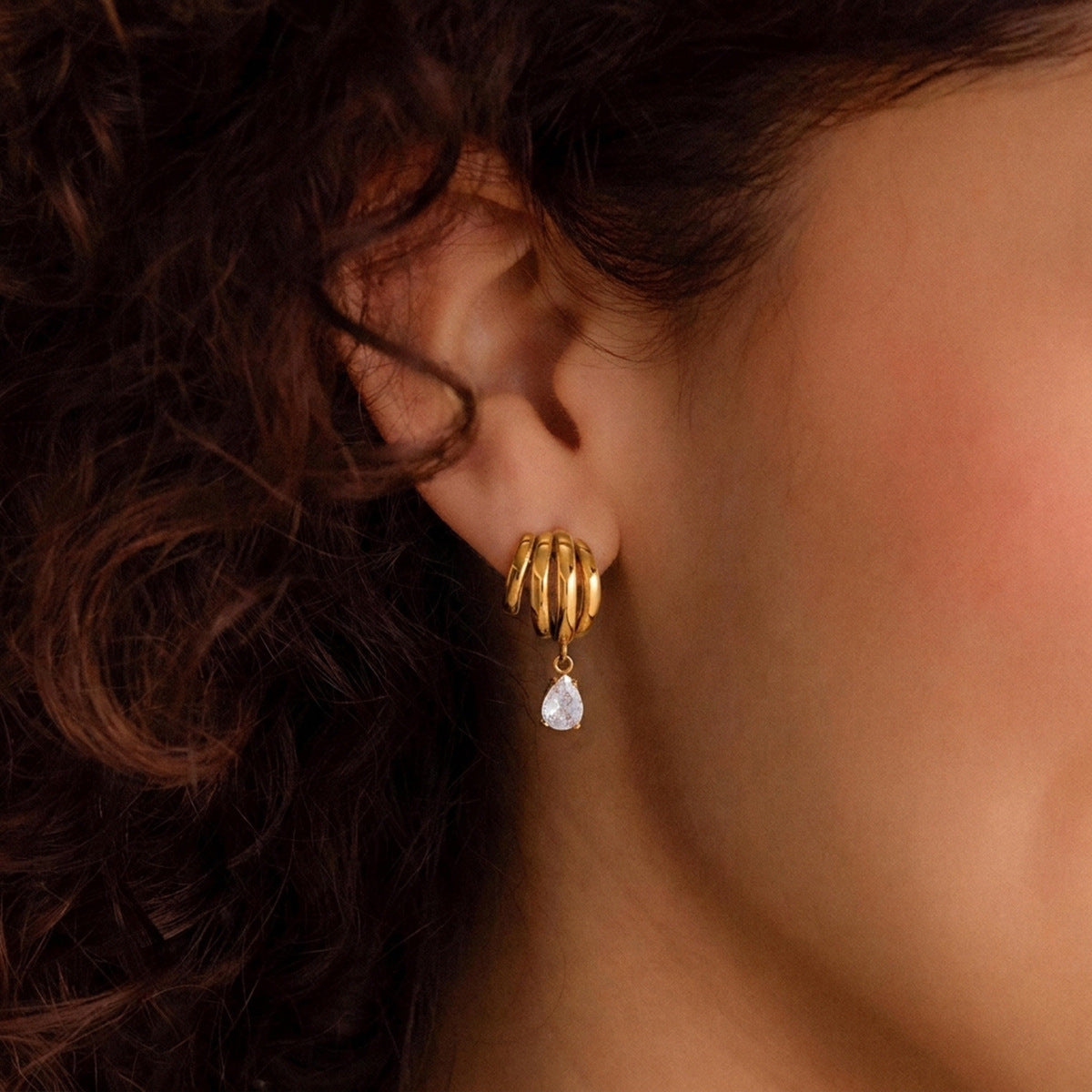 Gold tone multi-loop earring with clear teardrop on ear