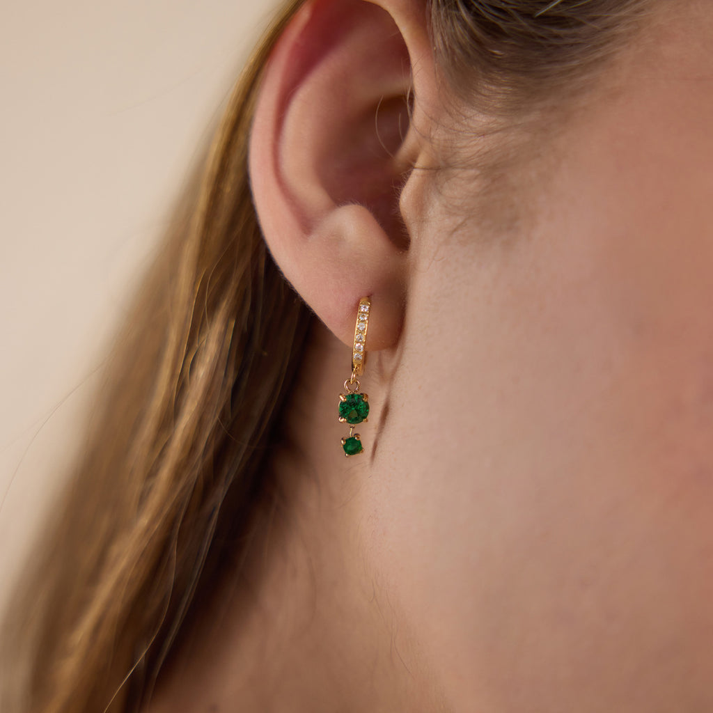 Gold tone hoop with two green stones shown on the ear