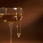 gold plated station necklace draped over a glass