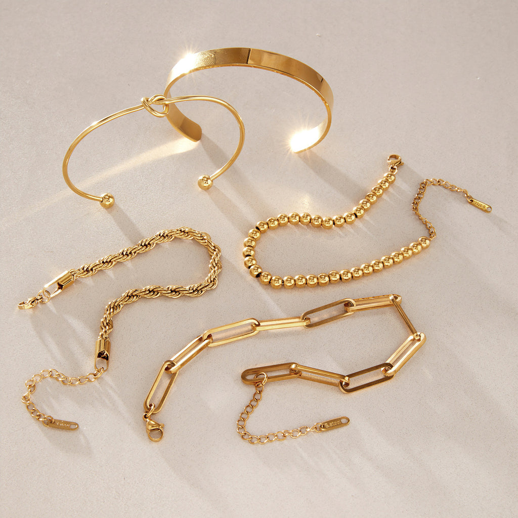 Five gold-tone bracelet styles arranged on stone
