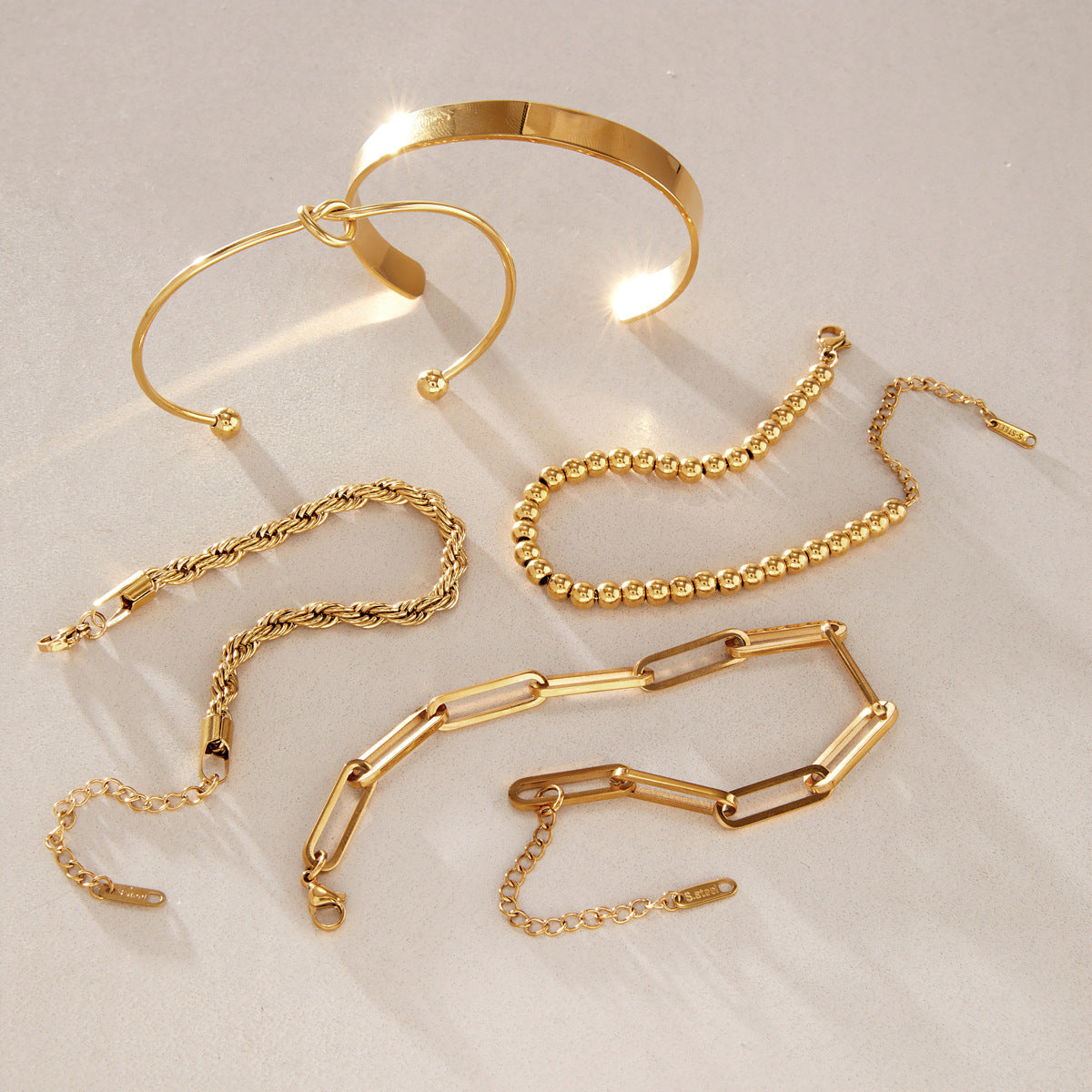 Five gold-tone bracelet styles arranged on stone