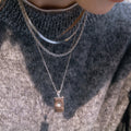 Gold plated three-strand star tag necklace worn over a knit top