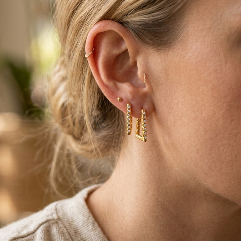 Gold-tone geometric hoop earrings worn on ear