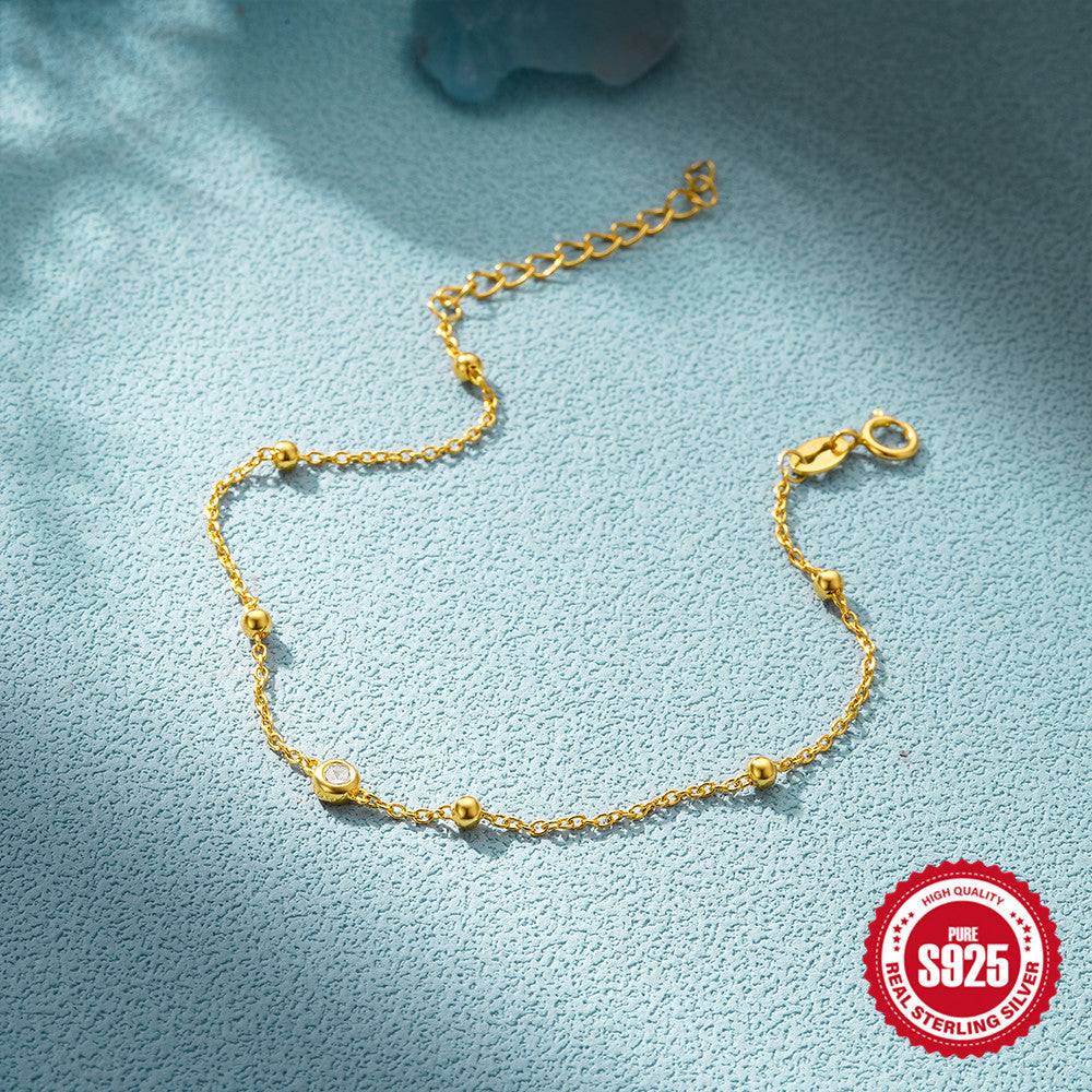 925 Sterling Silver Beaded Zirconia Station Bracelet — gold chain and clasp on blue fabric