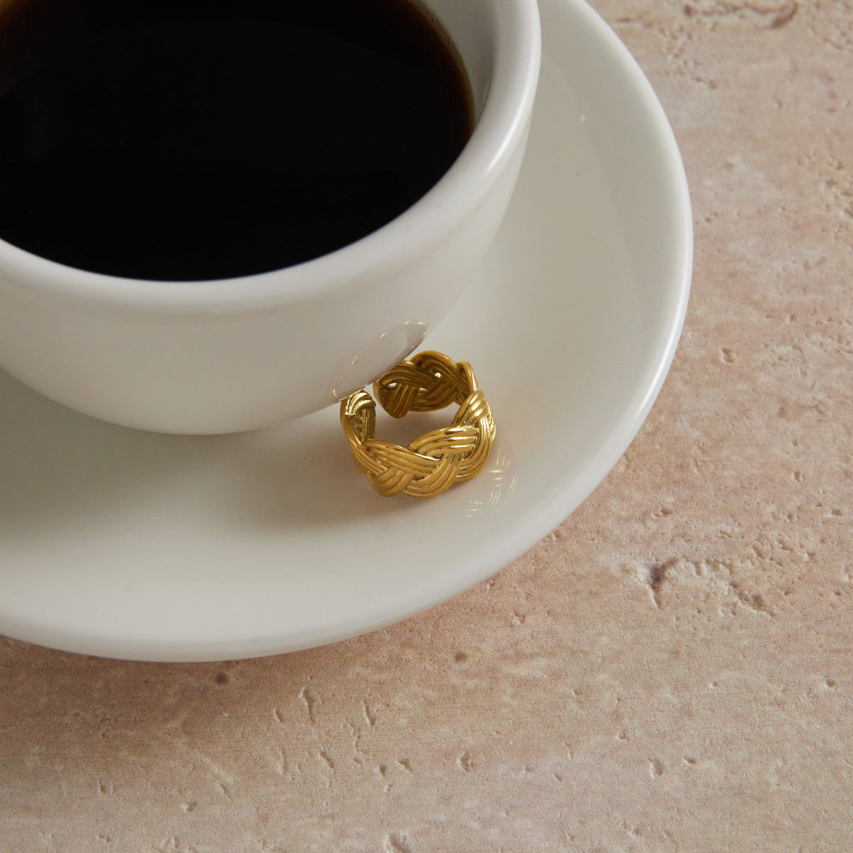 Open braided ring displayed beside a cup