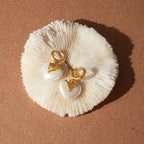gold plated stainless steel heart earrings arranged on a shell