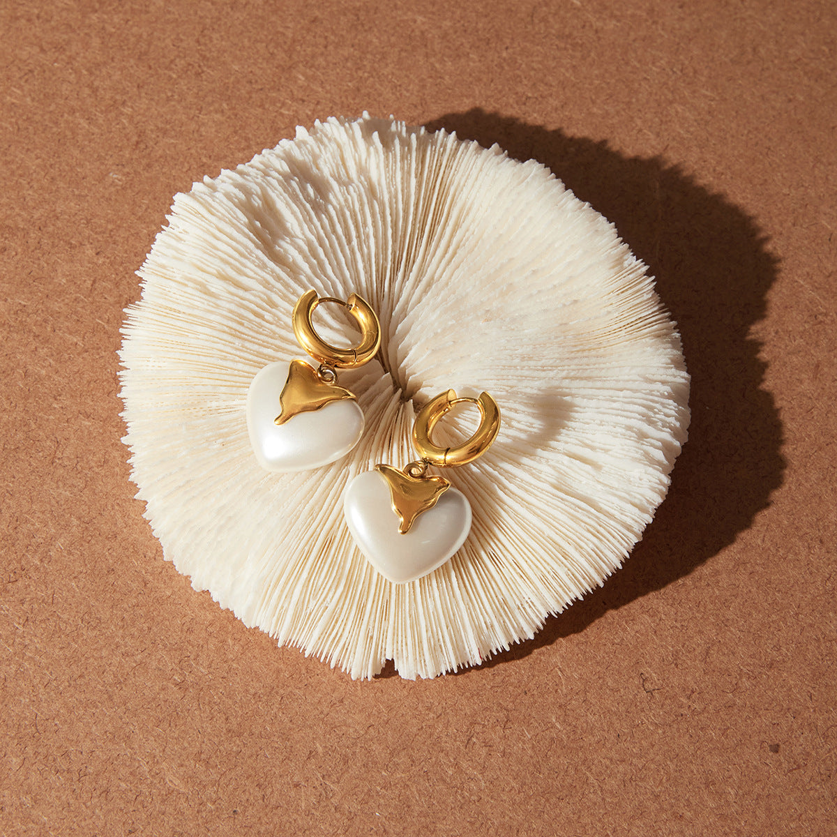gold plated stainless steel heart earrings arranged on a shell