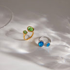 Gold-tone green and silver-tone blue rings on a pale surface