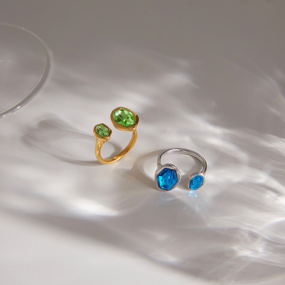 Gold-tone green and silver-tone blue rings on a pale surface