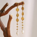 gold plated textured medallion pearl drop earrings hanging from a branch