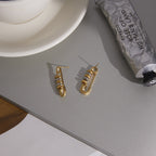 two-tone stainless steel safety-pin earrings displayed on a gray surface