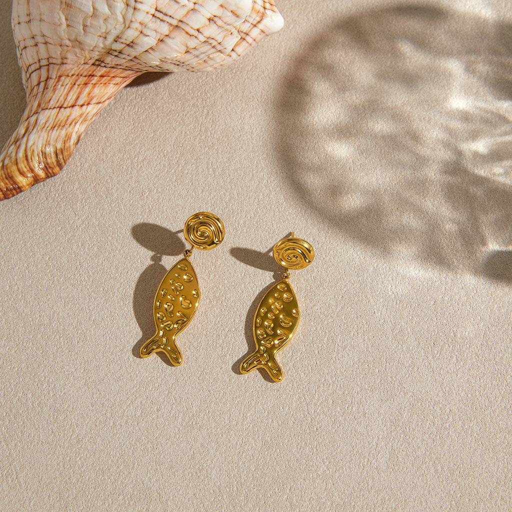 Pair of fish earrings beside a shell