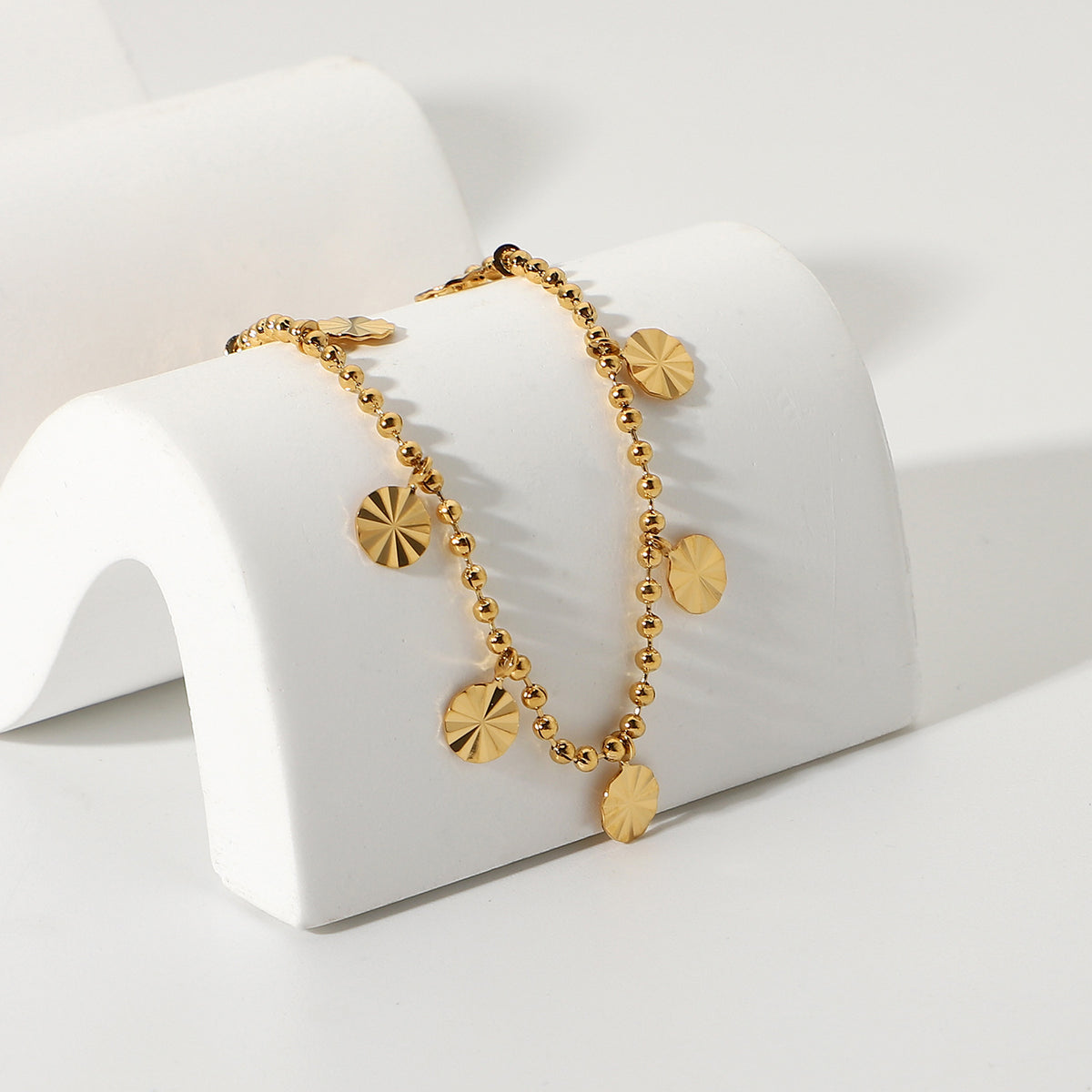 Disc charm anklet draped over a white curved display