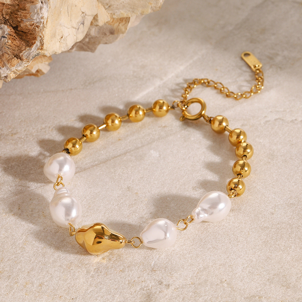 Gold ball and irregular white bead bracelet on a stone display