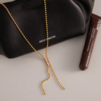 Gold plated beaded-detail Y chain laid on a dark accessory