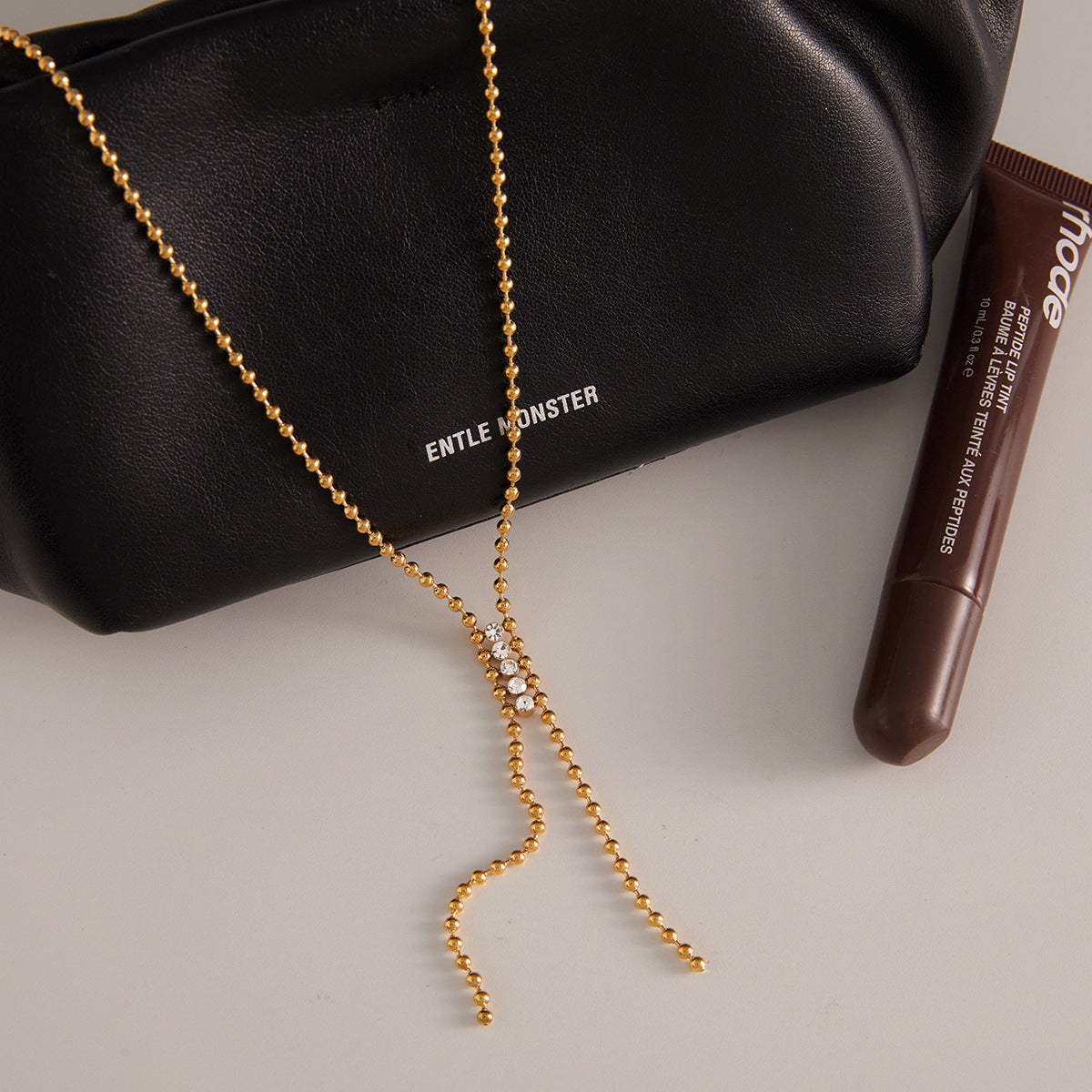 Gold plated beaded-detail Y chain laid on a dark accessory
